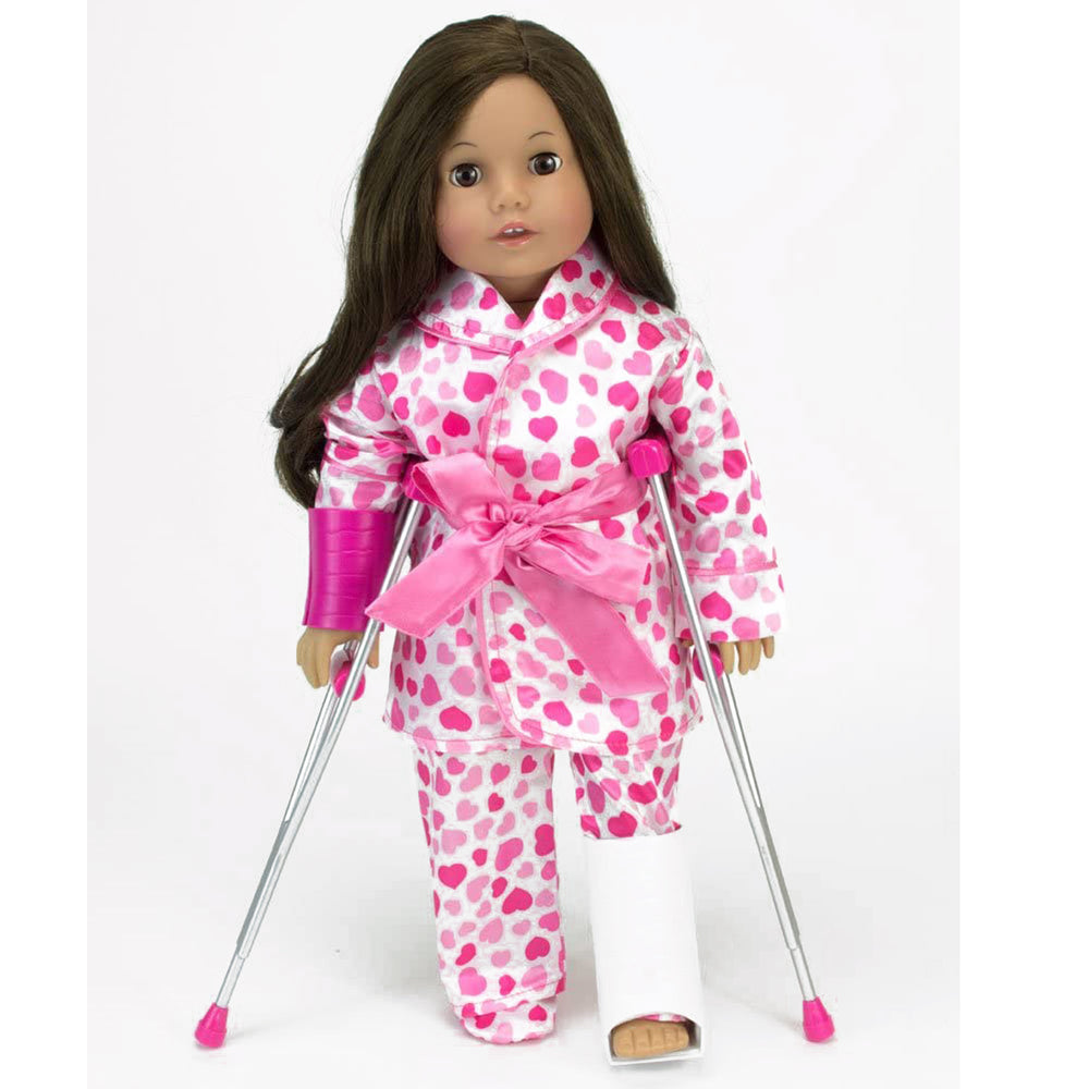 An 18" brunette doll dressed in pink hearts pajamas with a cast on her left leg, held up by crutches.