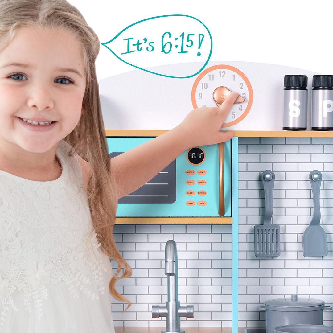 Young girl pointing to a clock reading 6:15 in a Teamson Kids Little Chef Santos Retro Wooden Kitchen Playset, Aqua/White.