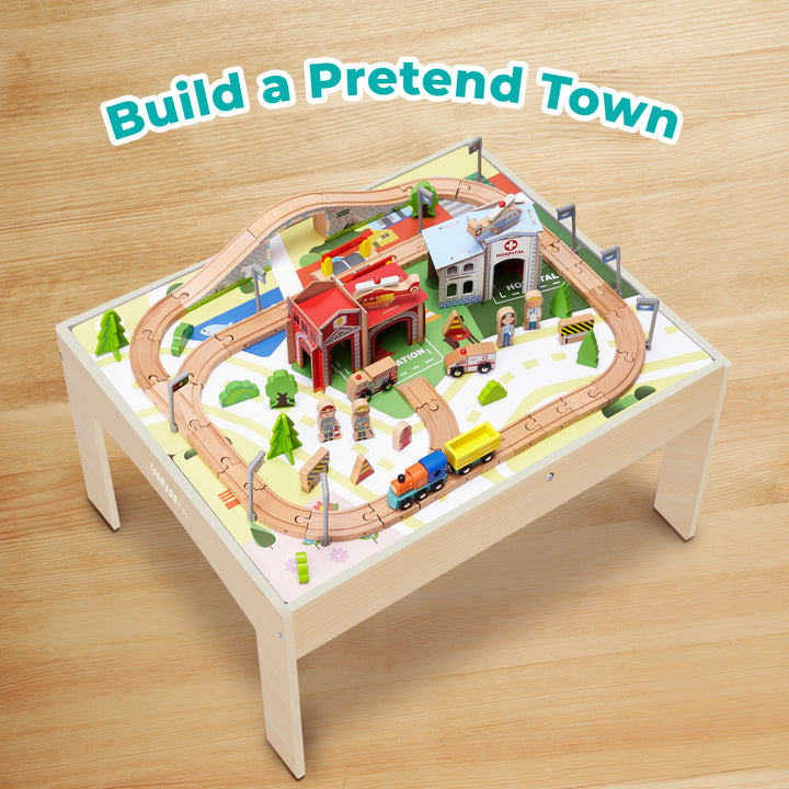 Teamson Kids Preschool Play Lab Toys Wooden Table with 85-pc Train and Town Set, Natural on a small table, featuring a track arrangement, buildings, trees, and miniature cars, inviting imaginative play.