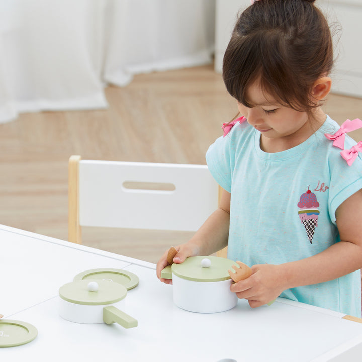 A young child enjoying kids play with a Teamson Kids Little Chef Frankfurt Wooden Cookware Play Kitchen Accessories set at a table designed with kid-friendly dimensions.