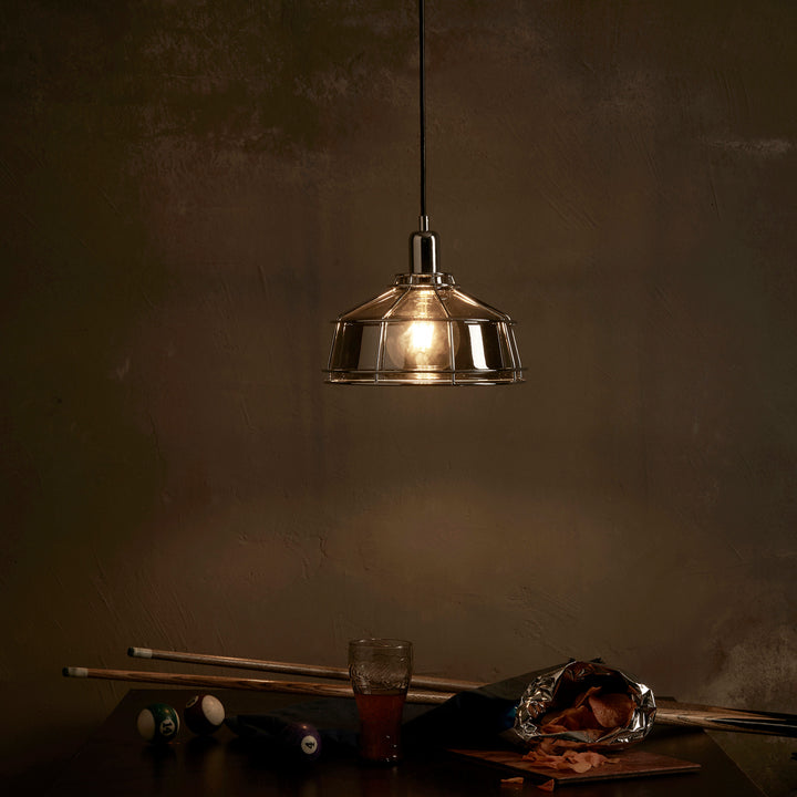 A dimly-lit room with a Teamson Home Presenza Metal Mini Pendant Lamp With Cage, Chrome shining over a pool cue, scattered billiard balls, and a drink on a table.