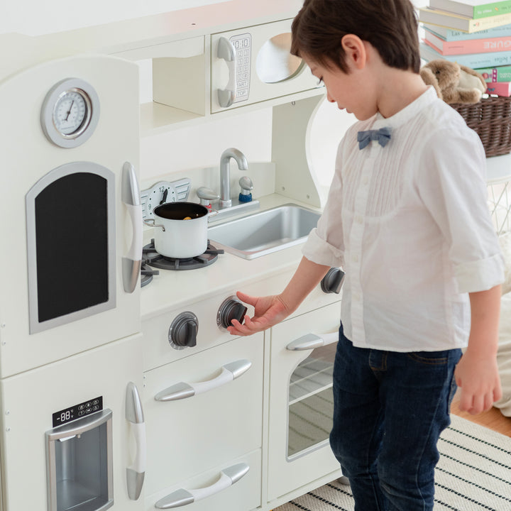A child playing with a Teamson Kids Little Chef Westchester Retro Kids Kitchen Playset, Ivory, including an interactive toy telephone.