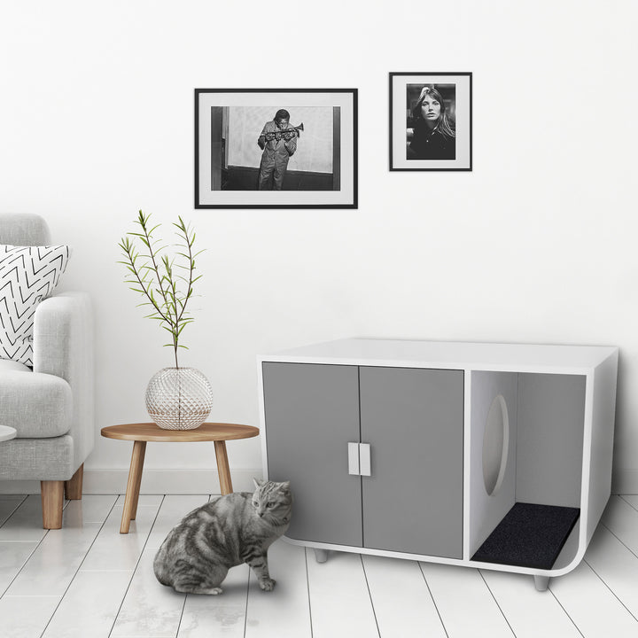 A cat standing next to a Teamson Pets Large Dyad Wooden Cat Litter Box Enclosure and Side Table, Alpine White/Gray in a stylish living room with black and white photographs on the wall.