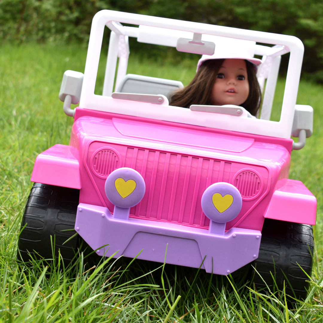 A brunette 18" doll driving a pink 4 x 4 beach cruiser in the grass.