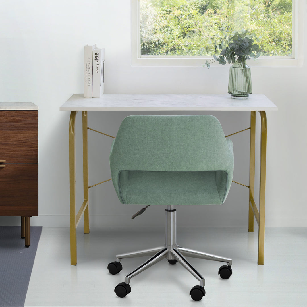 A desk and a Teamson Home Modern Fabric Office Chair with Adjustable Ergonomic Seat, Swivel Base, and Wheels, Mint/Chrome in a room with a window.