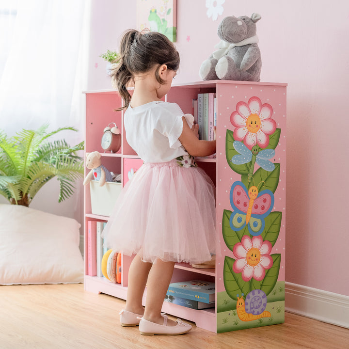 A little girl in a pink tutu standing next to a Fantasy Fields Kids Painted Wooden Magic Garden Adjustable Cube Bookshelf adjusting the books.