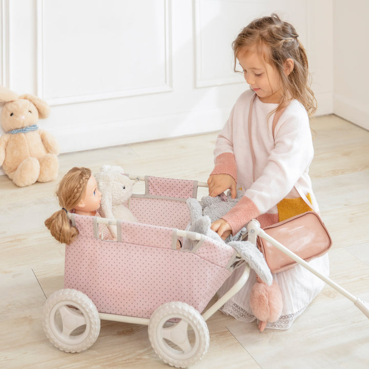 A little girl is playing with a Olivia's Little World Polka Dots Princess Baby Doll Wagon in pink.