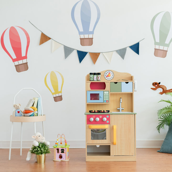 Teamson Kids Little Chef Florence Classic Play Kitchen with 5 Kitchen Accessory Toys, Wood Grain in front of a wall with hot balloon decals on the wall.