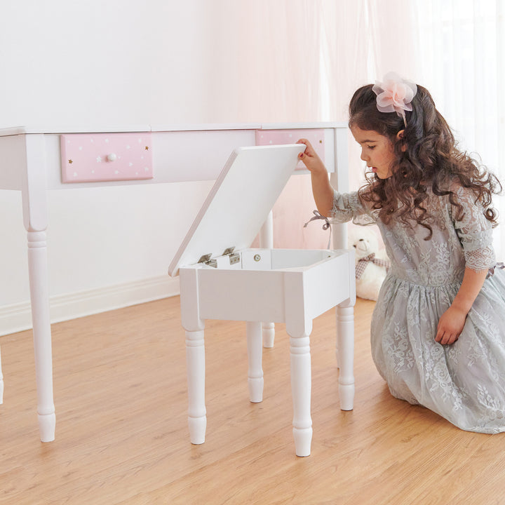 A little girl looing into the stool' storage space of her pink and white vanity table.