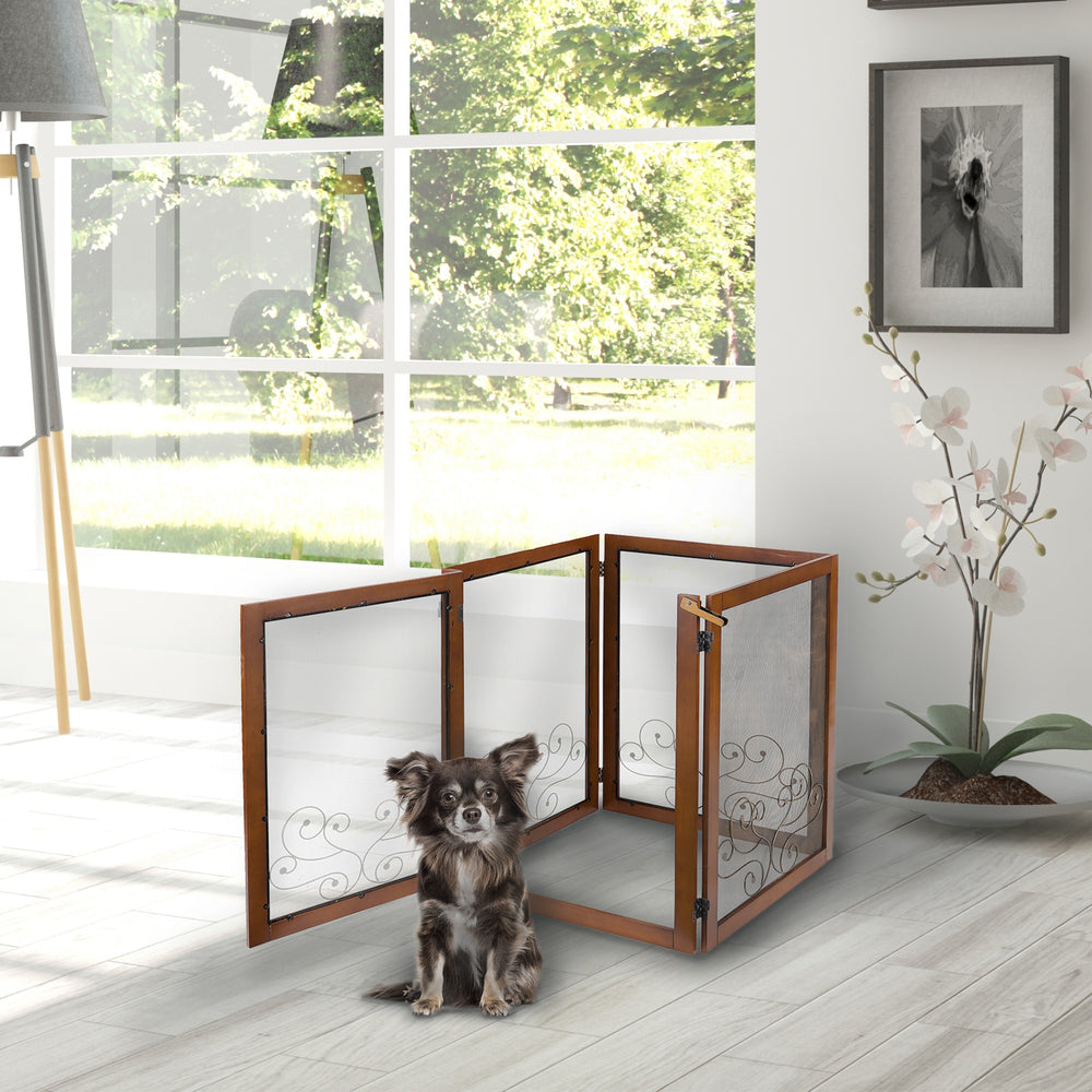 A small dog sits next to a Decorative Dog Gate with 4 Screened Panels and Ornamental Scrollwork in a bright room with a view of trees outside.