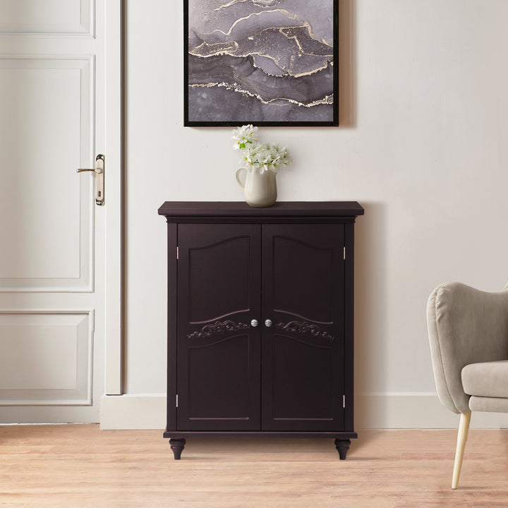 Teamson Home Versailles Dark Espresso Floor Cabinet with ornate detailing, positioned against a wall next to a closed door, with a vase of flowers on top.