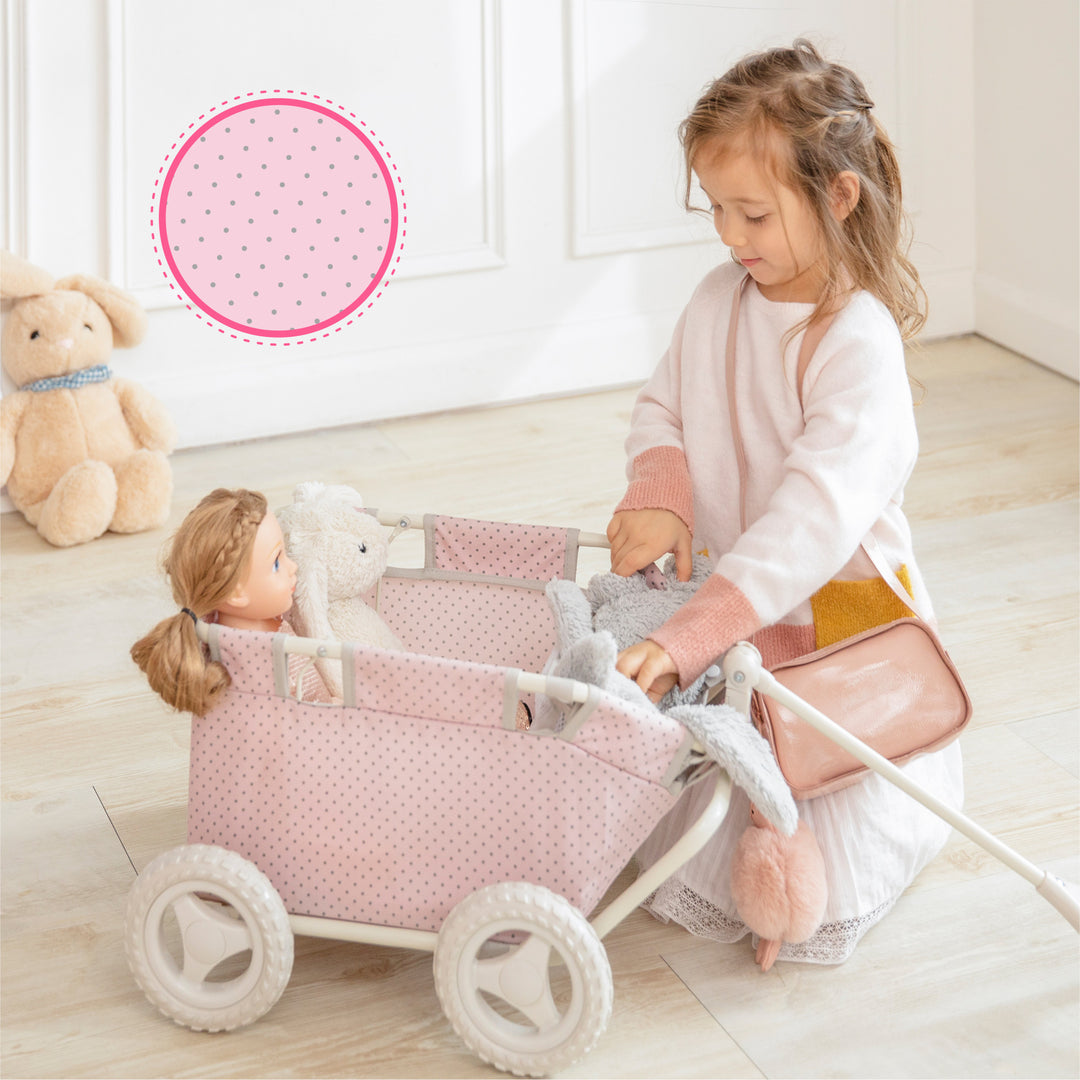 A little girl is playing with Olivia's Little World Polka Dots Princess Baby Doll Wagon with a close-up of the material, pink with gray polka dots.