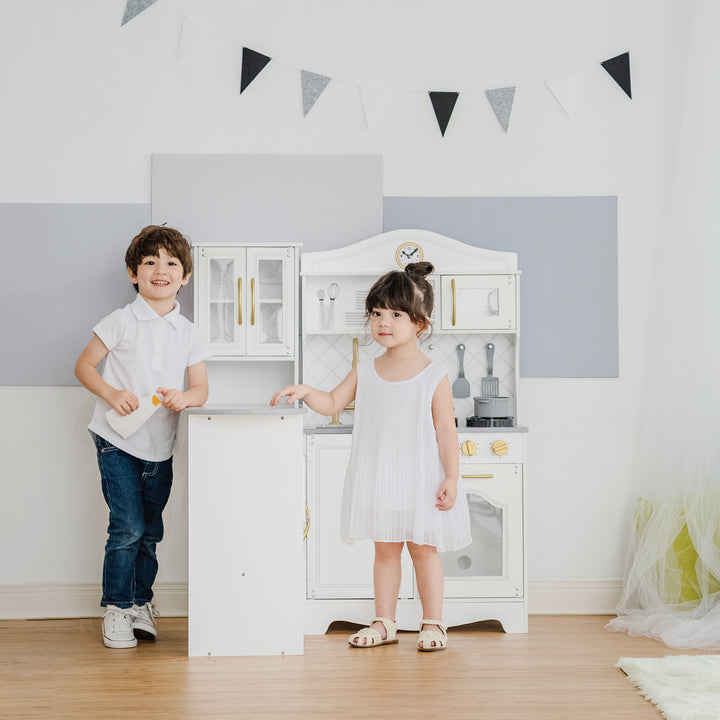 A little boy and little girl standing on either side of the counter portion of the play kitchen.