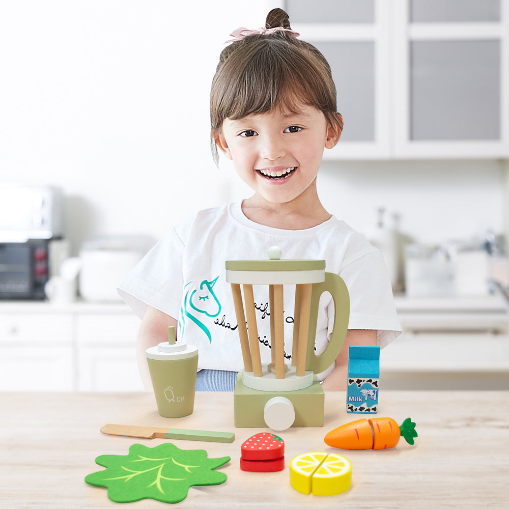 A smiling child playing with a Teamson Kids Little Chef Frankfurt Wooden Blender Play Kitchen Accessories, Green and assorted pretend ingredients.