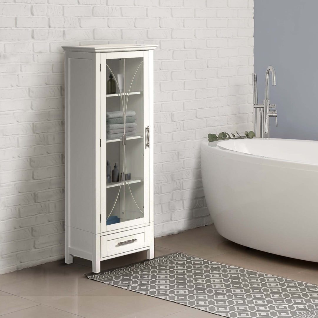 White Teamson Home Delaney Free Standing Tall Linen Cabinet Tower with Glass Panel Door with a Storage Drawer next to a freestanding bathtub in an industrial bathroom
