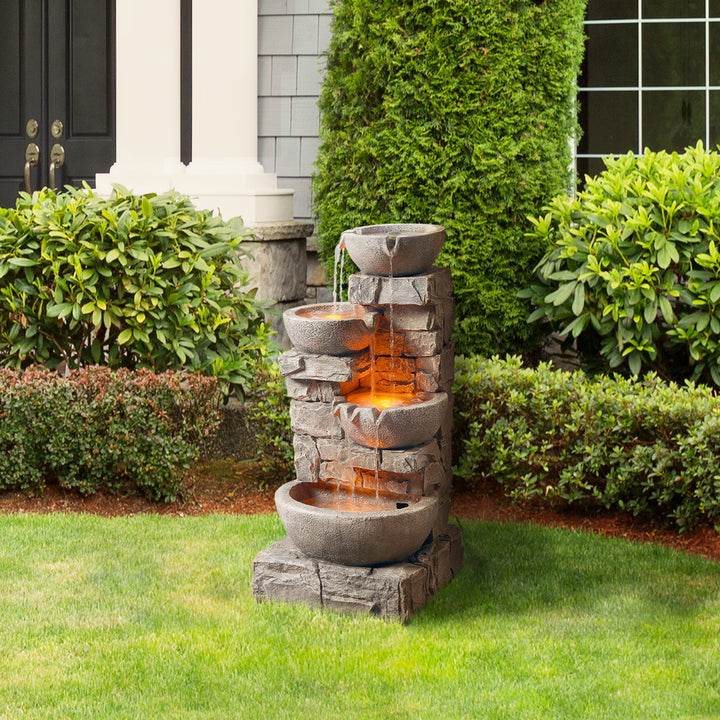 A Teamson Home Outdoor Cascading Bowls & Stacked Stone water fountain, Gray, sat next to some hedges in front of a house