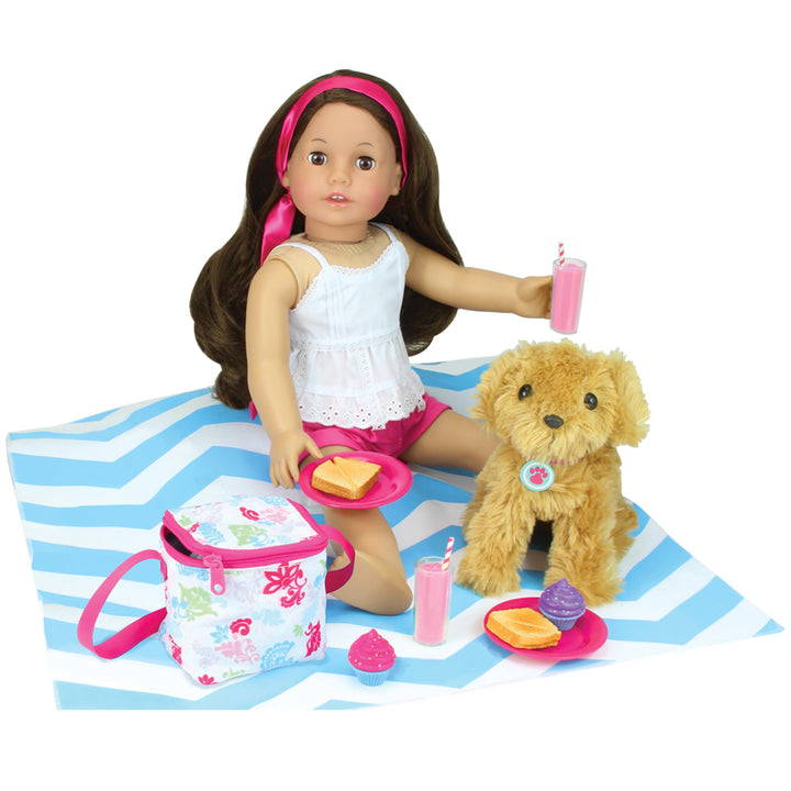 An 18" doll with brunette hair sitting on the picnic blanket with her puppy, with a drink in her hand and a sandwich on a plate next her other hand.