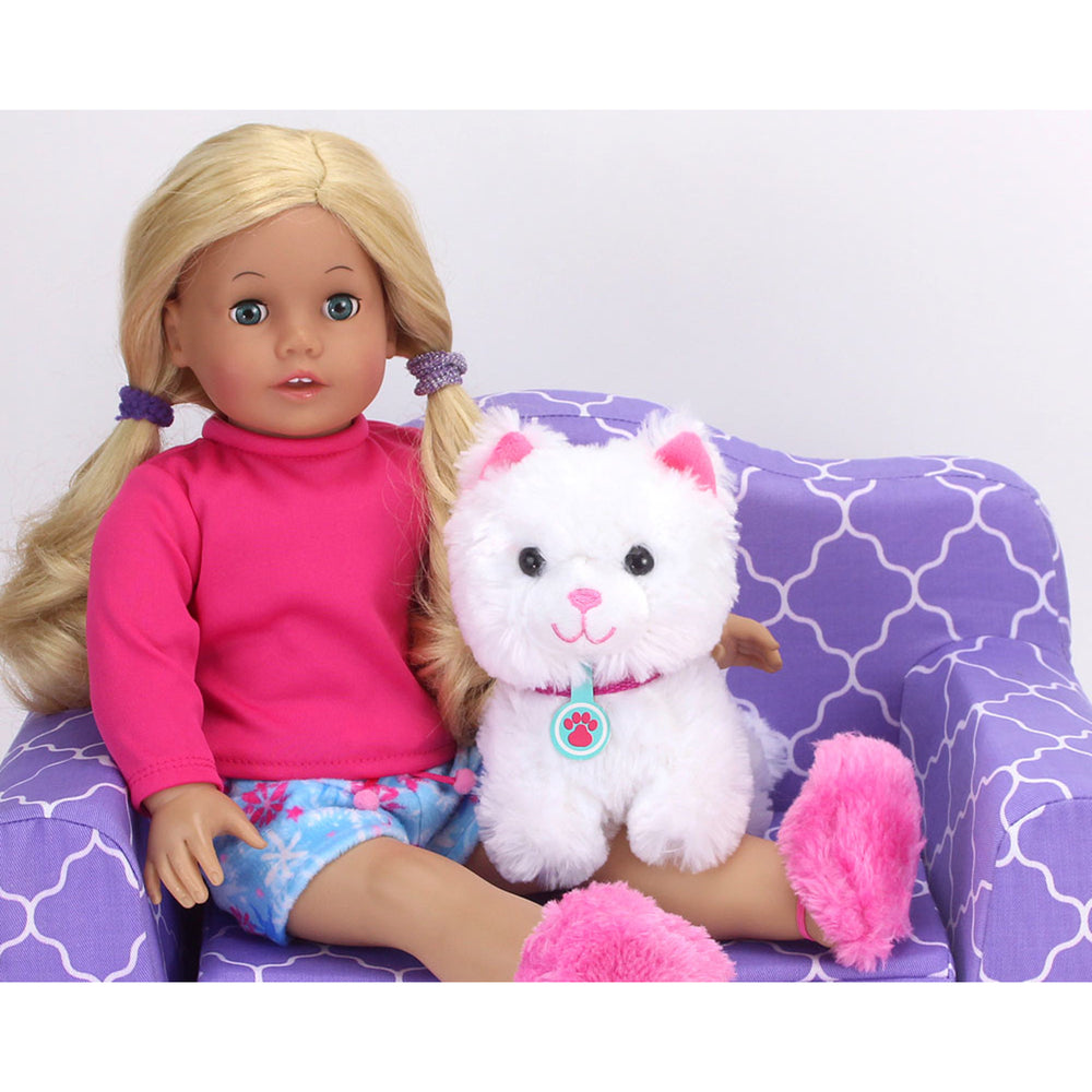 An 18" doll with blonde hair and blue eyes dressed in a pink long sleeved shirt and blue shorts sits on a purple couch with her white kitten.