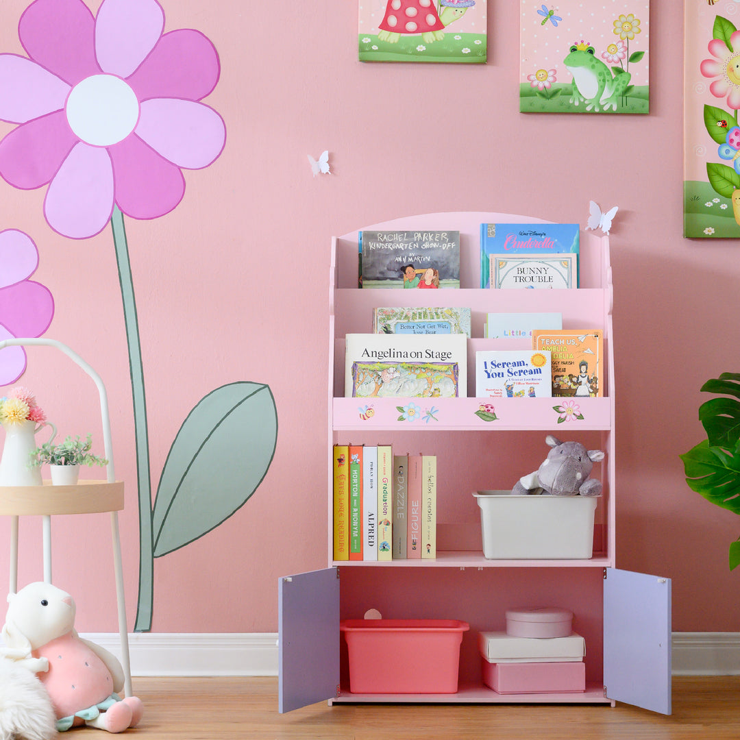 A children's room with a Fantasy Fields Magic Garden Kids 3-Tier Wooden Bookshelf with Storage, Multicolor and stuffed animals.