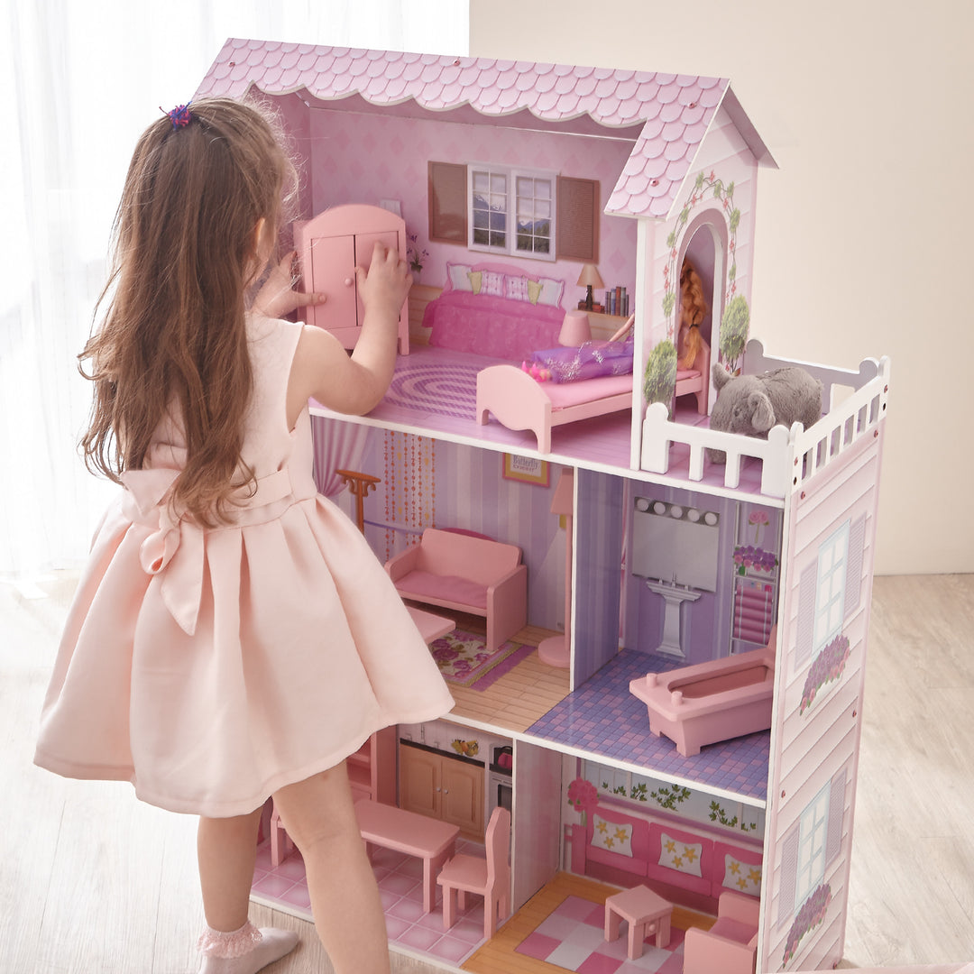 A little girl playing with Olivia's Little World Dreamland Tiffany Dollhouse with 12 Accessories, Pink/Purple, featuring wooden construction.