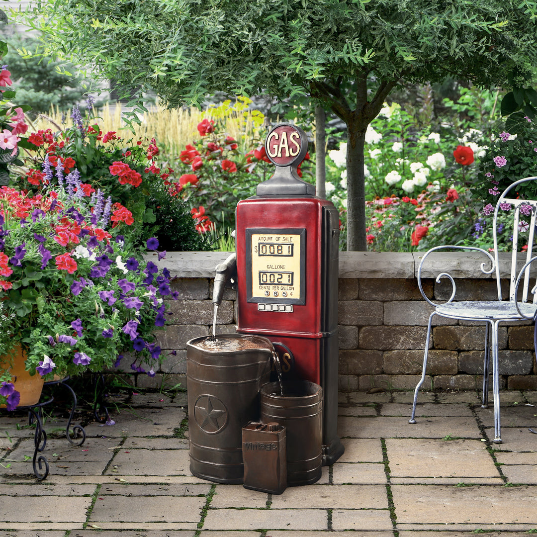 Teamson Home Outdoor Vintage Gas Pump water fountain surrounded by a lush garden with flowers, a brick patio, and cast iron chairs