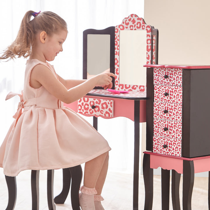 A little girl sitting on a pink and black Fantasy Fields Gisele Leopard Print Vanity Playset.