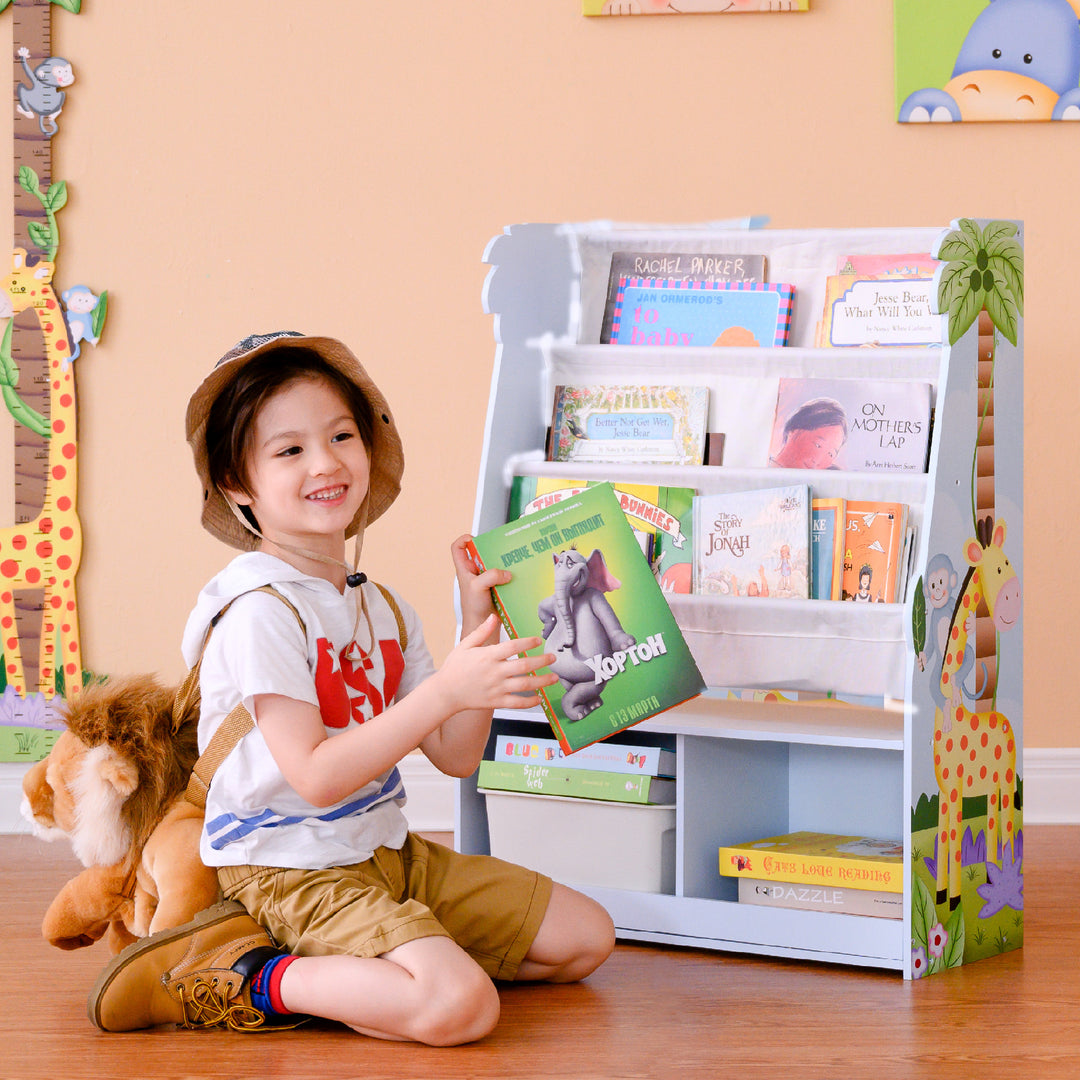 A child sitting on the floor in front of a Fantasy Fields Kids Sunny Safari Wooden Display Bookshelf with Storage Cubbies, Multicolor.