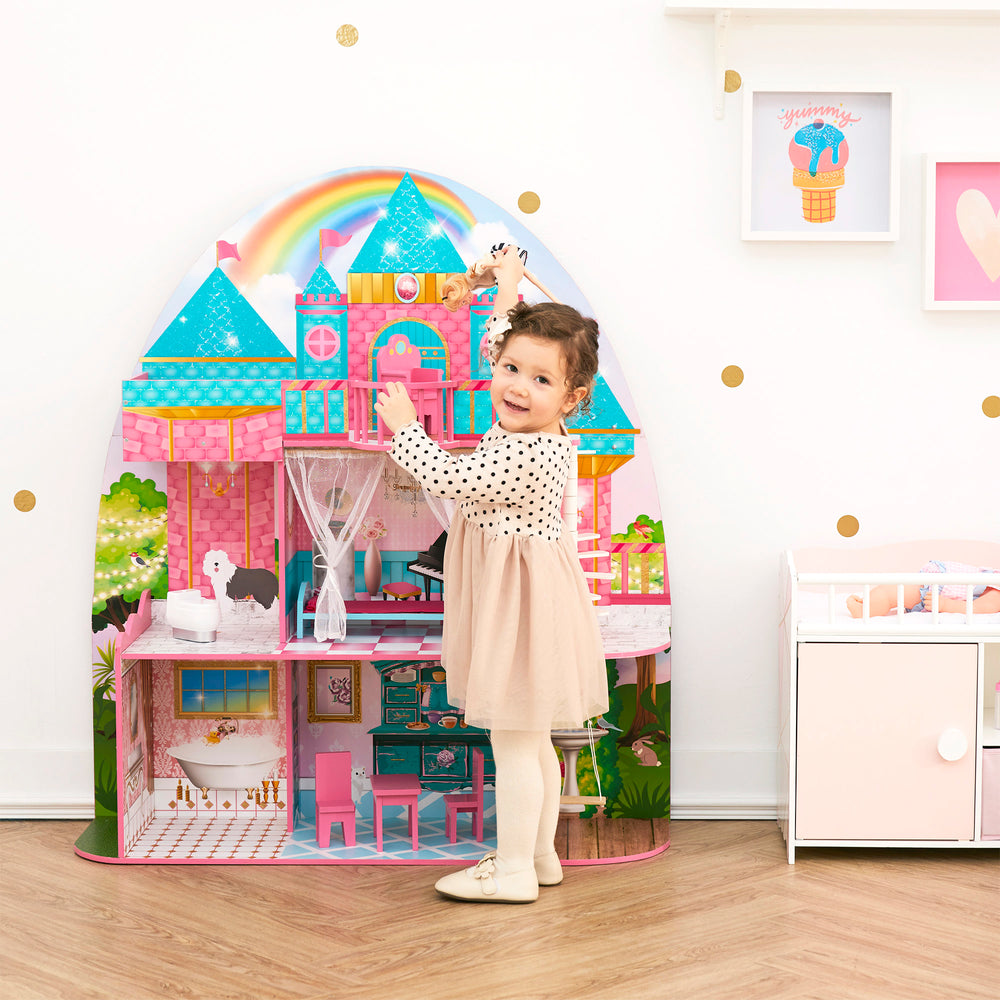 A little girl standing next to a brightly-colored, illustrated with details, dollhouse.