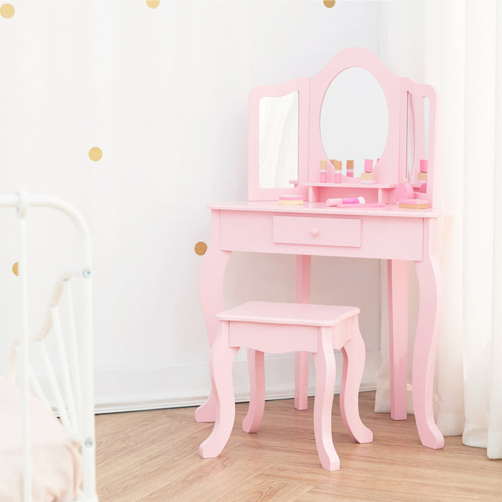 apink vanity table and stool with a tri-fold mirror in the corner of a white bedroom with gold polka dots.