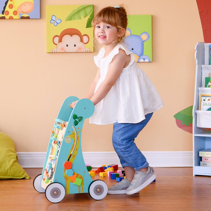 A young girl pushing a Teamson Kids Preschool Play Lab Wooden Baby Walker and Activity Station, Natural/Blue filled with blocks in a colorful playroom.