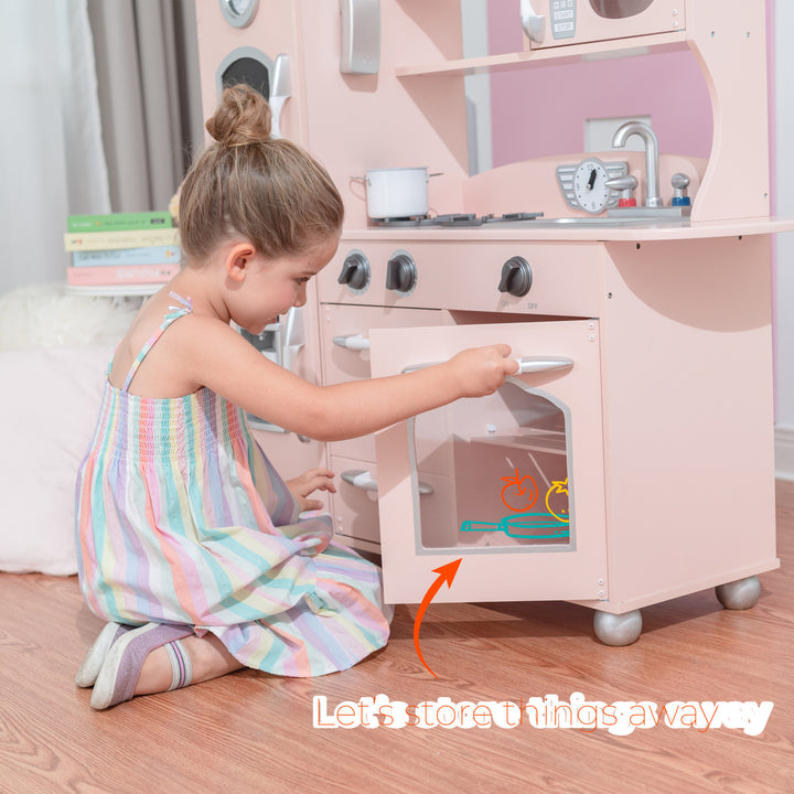 A young girl kneels while playing with a Teamson Kids Little Chef Westchester Retro Play Kitchen, Pink, putting items inside the oven of her kids play kitchen set.