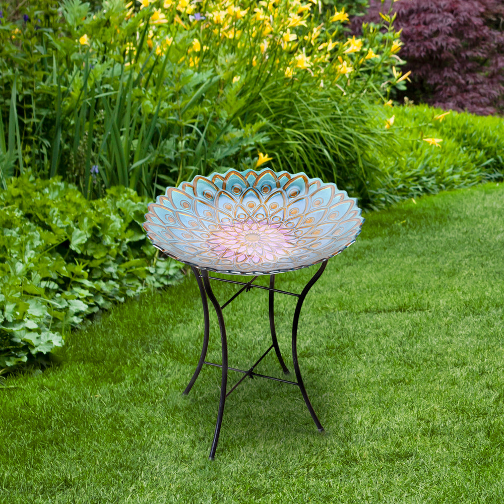 A Teamson Home 18" Glass Mosaic Flower Bird Bath with Stand, Multicolor in a garden.
