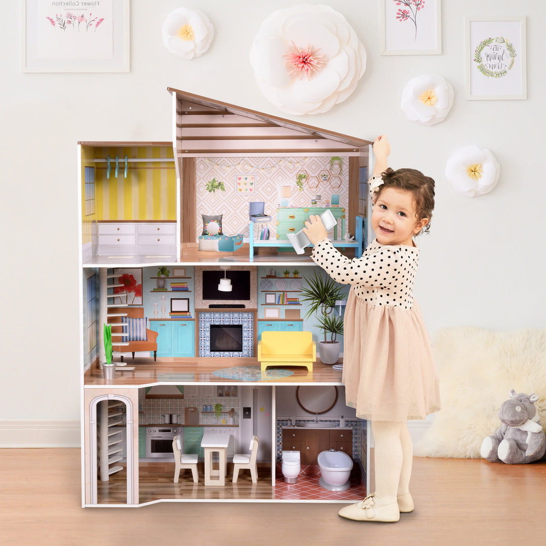 A little girl standing in front of Olivia's Little World Wooden Dreamland Mediterranean Dollhouse Set.