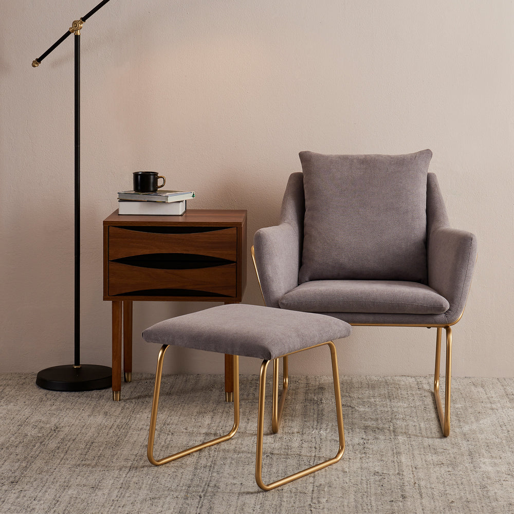Miller gray armchair and ottoman with gray fabric and gold framework sat next to an end table and floor lamp.