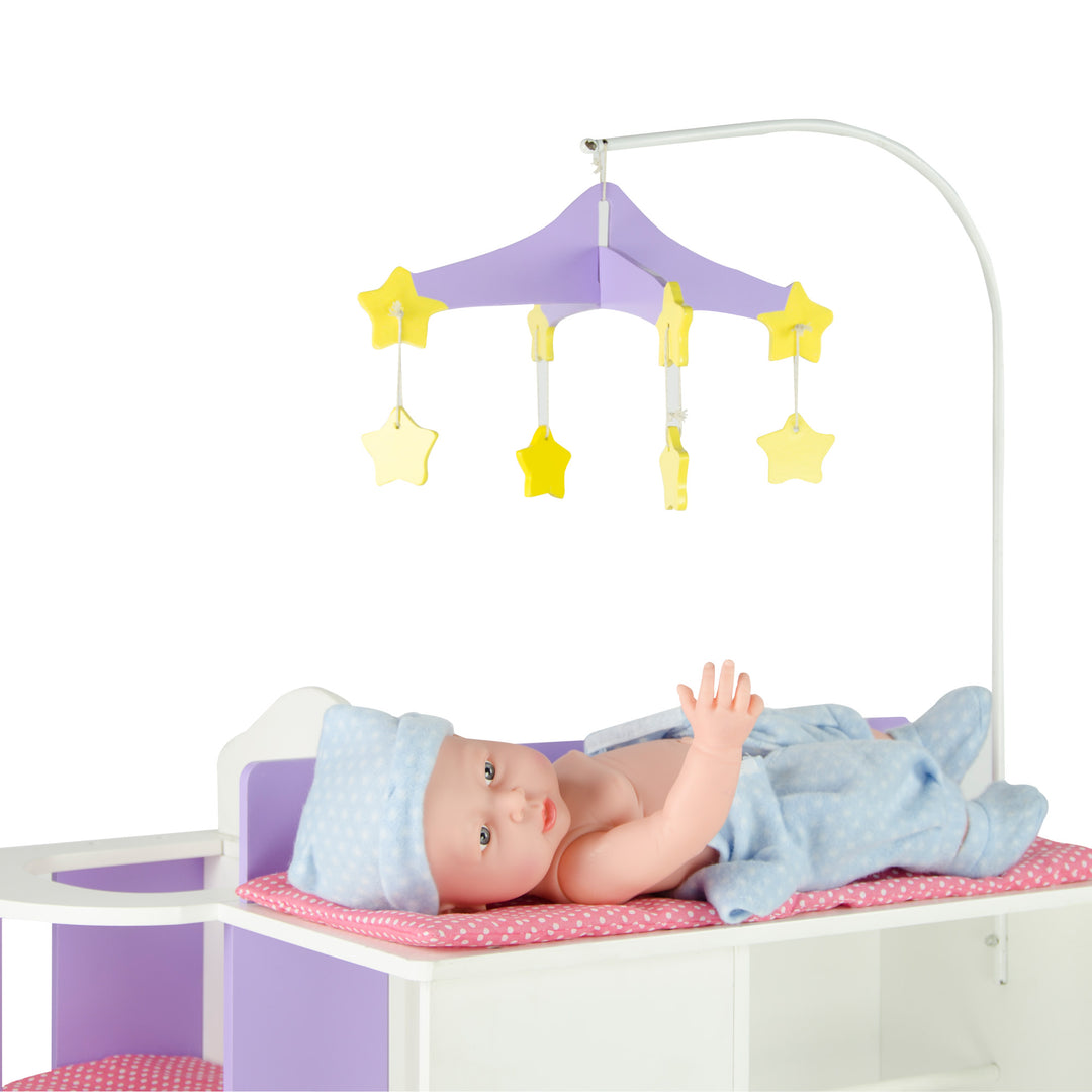 A photo of a baby doll laying on the changing table portion of the baby doll changing station with a mobile hanging overhead.