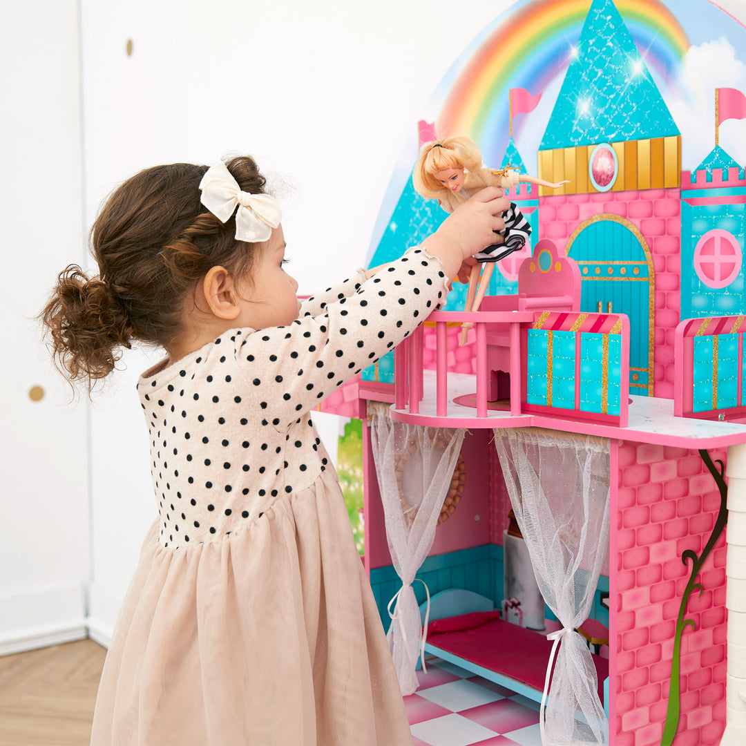 A little girl reaches up to put her doll in the throne in the balcony of her vividly-colored castle dollhouse.