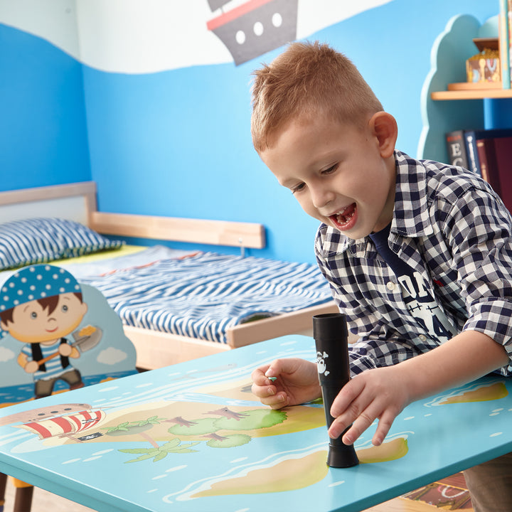A little boy balancing a black telescope on top of a child-sized table with black legs and a light blue tabletop with a pirate-themed illustration.