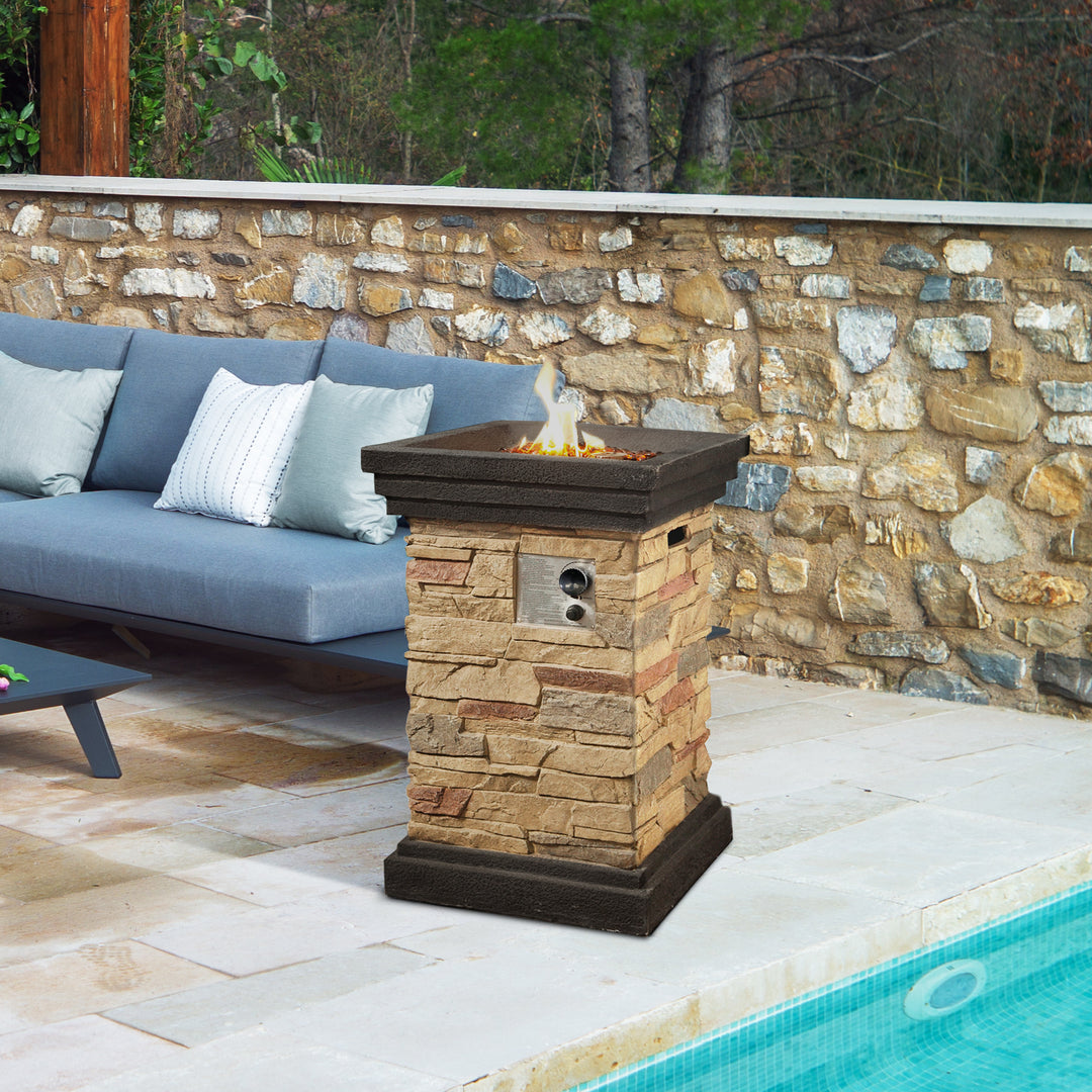 Teamson Home 20" Outdoor Square Faux Slate Propane Gas Fire Pit beside an outdoor pool with a stone facade, adjacent to a couch with cushions.