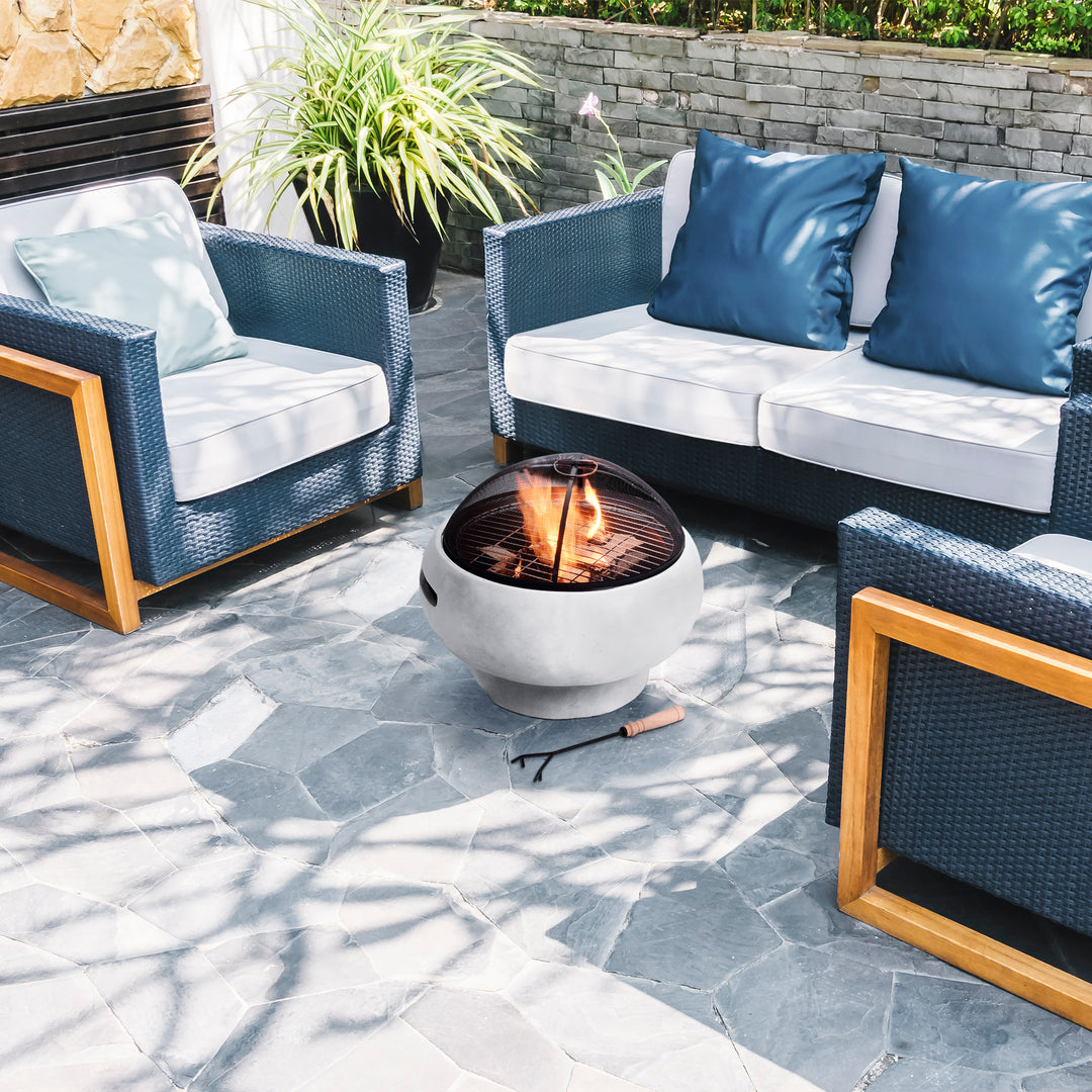 An outdoor seating area with modern furniture and a Teamson Home 21" Outdoor Round Stone Wood Burning Fire Pit with Faux Concrete Base, Gray centerpiece.