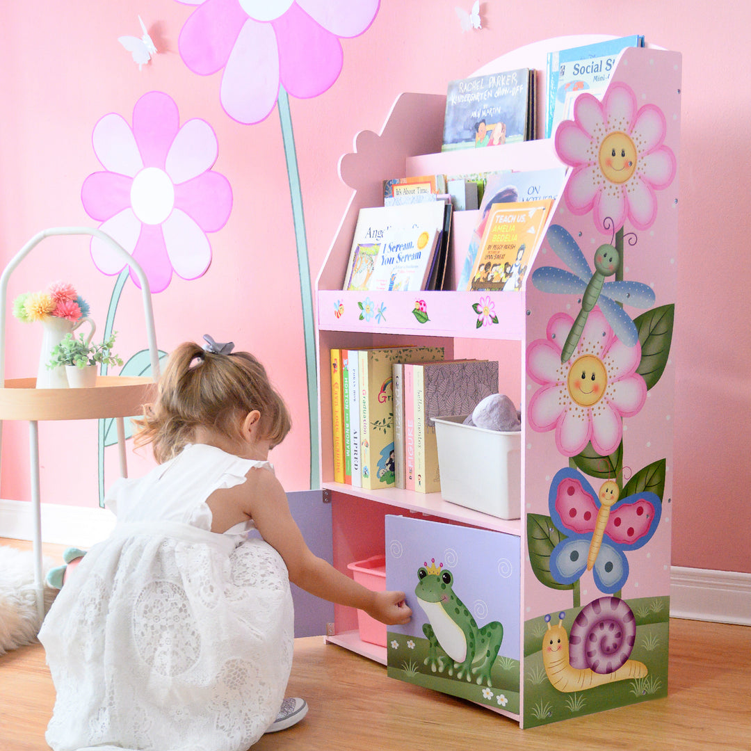 A little girl playing with a Fantasy Fields Magic Garden Kids 3-Tier Wooden Bookshelf with Storage, Multicolor.