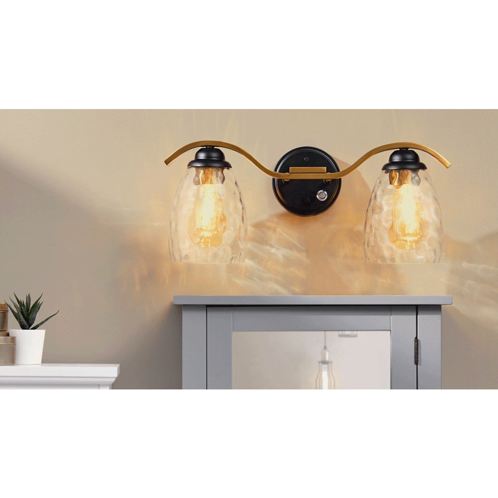 Heidi 2-Light Bathroom Vanity Wall Sconce Light with 3-Stage Touch Dimmer & Clear Hammered Glass Cloche Shades, Black/Brass arms above a gray console table with ambient lighting casting a warm glow on a beige wall.